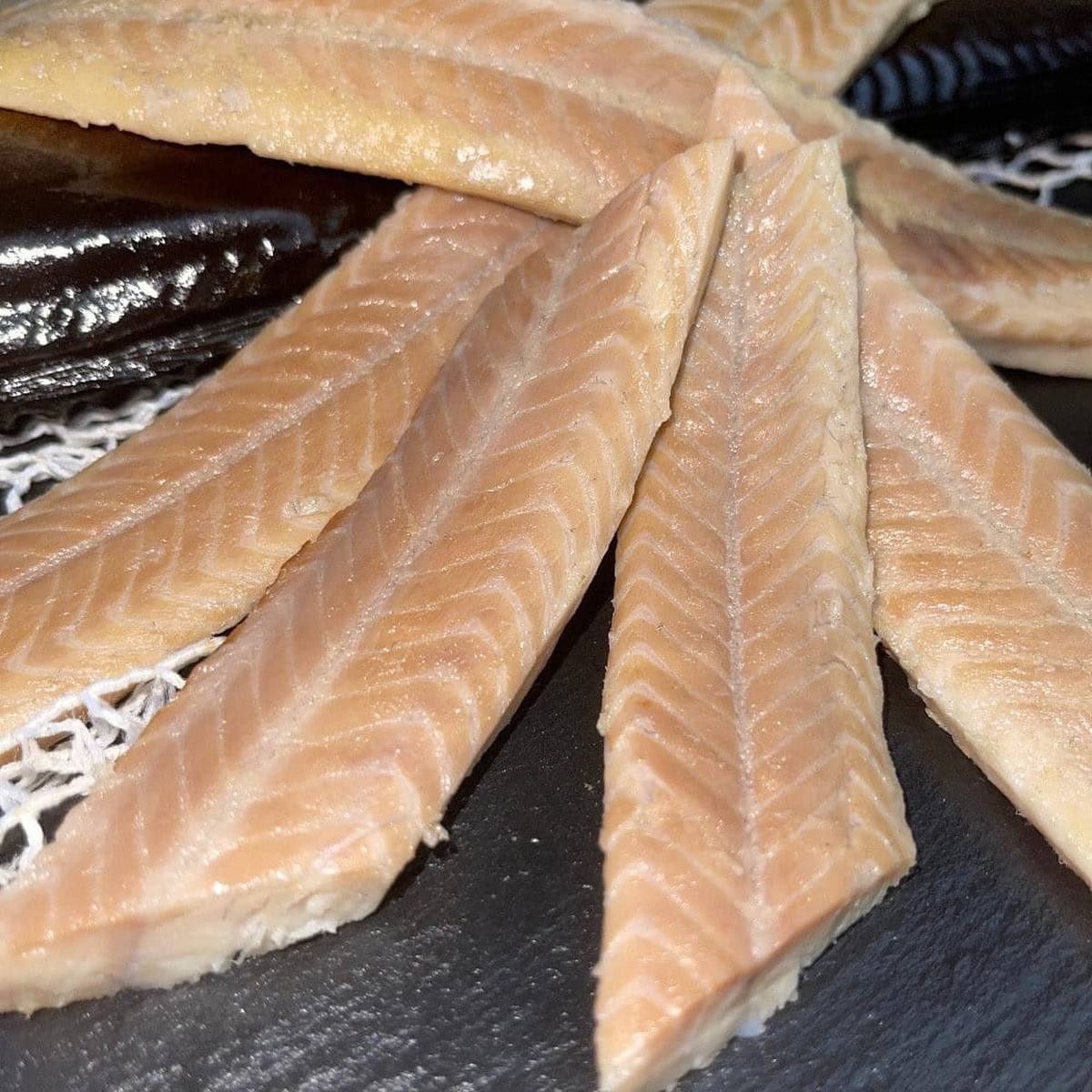  Heißgeräucherte Aalfilets ohne Haut, fächerförmig auf dunklem Schiefer ausgebreitet, im Hintergrund ein ganzer Räucheraal.