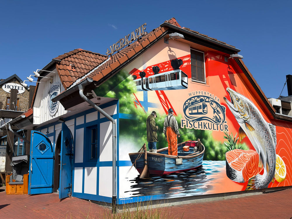 Außenansicht der Wuppertaler Fischkultur in der Schmiedestraße 57: Fachwerkhaus mit blauen Türen und großem Wandbild mit Schwebebahn, Fischern und Lachs