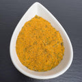 Bratfischwürzer in weißer Schale auf schwarzem Schiefer: orangefarbene Würzmischung mit grünen Kräutern.