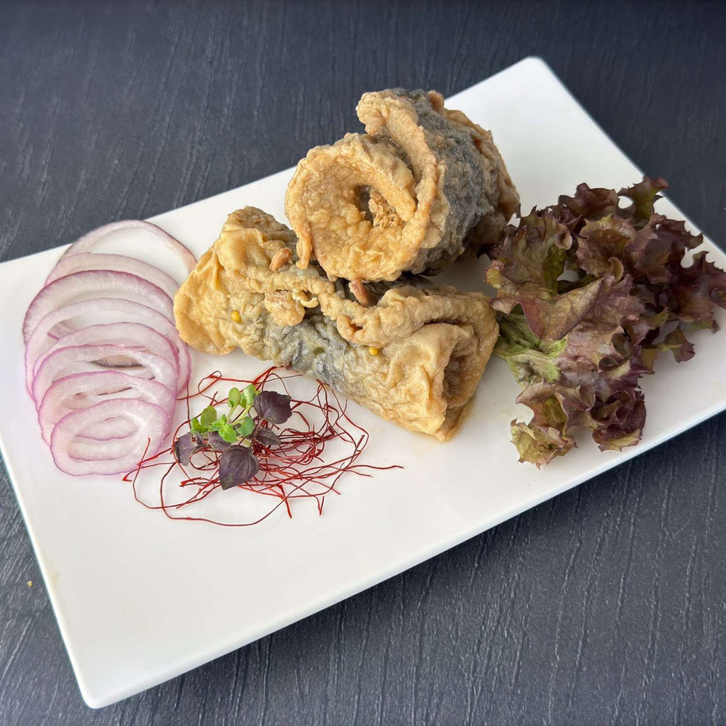 Zwei Bratrollmöpse auf weißer Platte: goldbraun gebratene, gerollte Heringsfilets, daneben rote Zwiebelringe und Salat als Deko.
