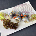 Drei Bremer Gabel-Rollis auf weißer Platte: kleine gerollte Heringsfilets mit Gewürzgurke, Senfsaat und Karotten, daneben Zwiebelringe und Salat als Deko.