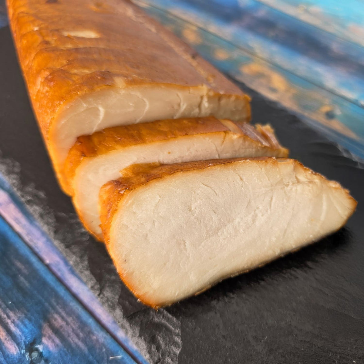 Heißgeräucherte Buttermakrele mit goldbrauner Haut, in Scheiben geschnitten, auf schwarzer Schieferplatte – saftiges, weißes Fleisch.