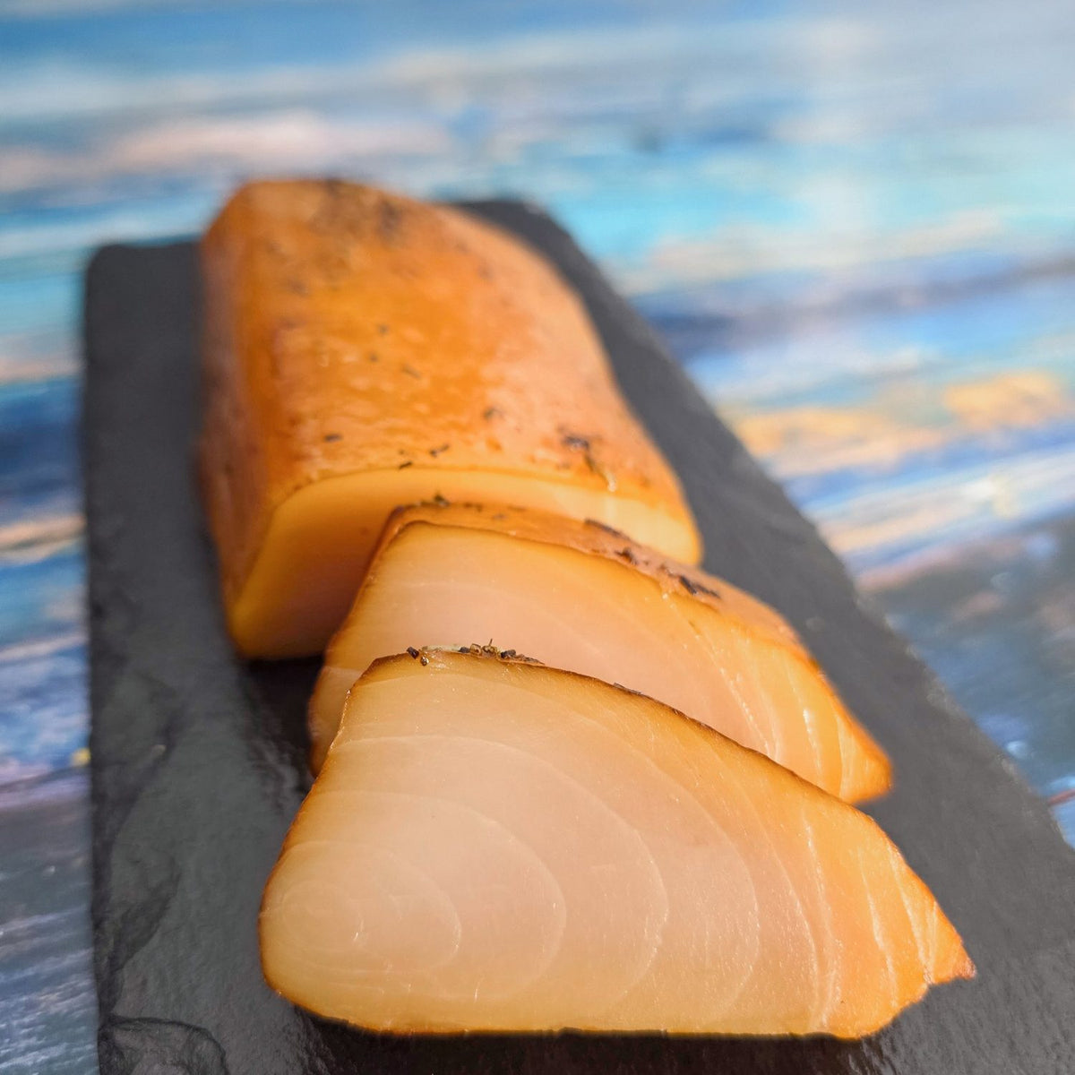Kaltgeräucherte Buttermakrele, in Scheiben geschnitten, auf schwarzer Schieferplatte – zartes, glasiges Fleisch mit Kräutern.