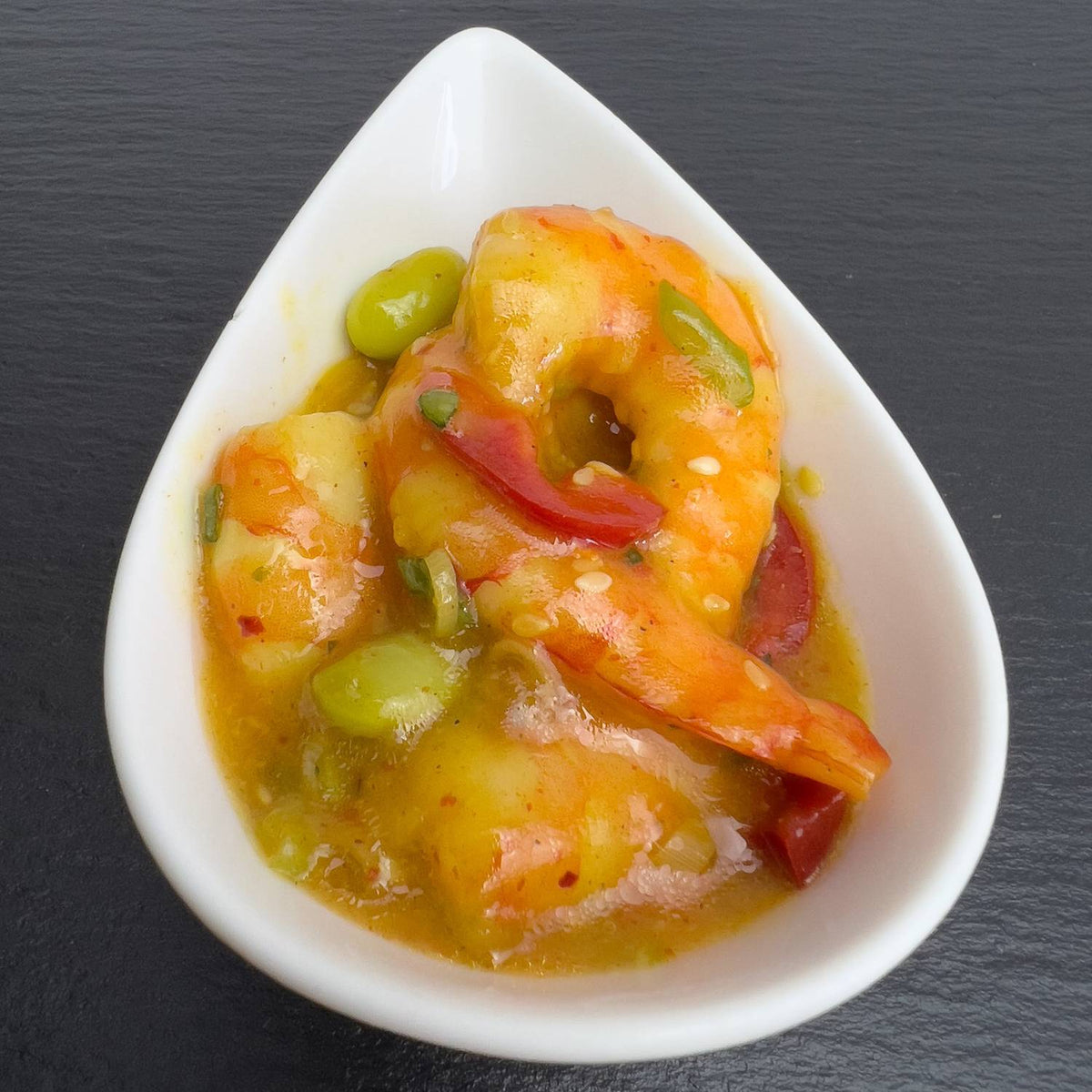 Chili-Garnelen in weißer Schale auf schwarzem Schiefer: Garnelen in fruchtig-scharfem Dressing mit Paprika, grünen Sojabohnen und Sesam.