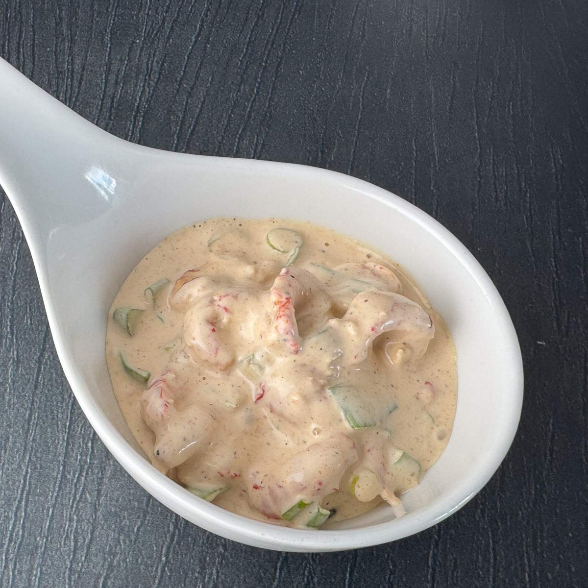Flusskrebssalat Asia in weißer Porzellanschale auf dunklem Untergrund: Flusskrebsfleisch in cremiger Cocktailsauce mit Lauchzwiebeln.