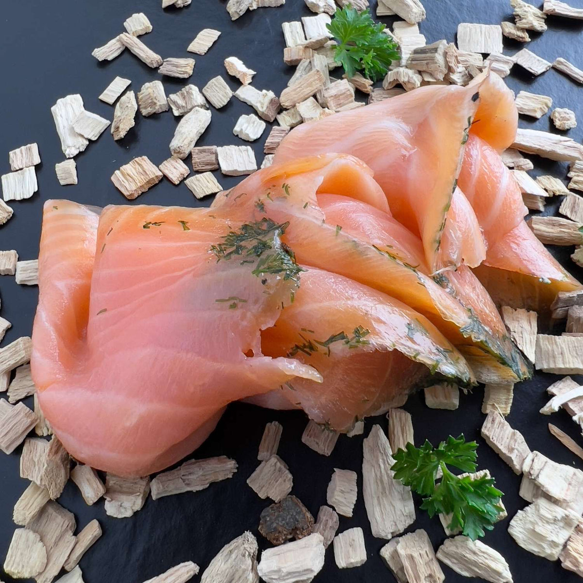 Graved Lachs in lockeren Scheiben mit Dill, dekoriert mit Holzchips und Petersilie. Die Chips sind nur Deko, denn gebeizter Lachs wird nicht geräuchert.