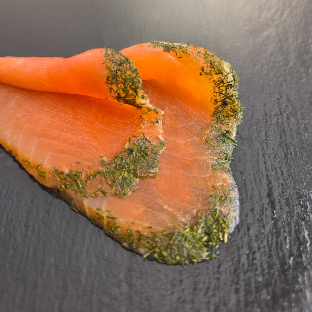 Graved Lachs auf dunklem Schiefer: hauchdünne, von Hand geschnittene Scheiben mit einem Rand aus frischem Dill, nach nordischer Art gebeizt.