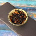 Hijiki-Algensalat in grüner Keramikschale auf Schieferplatte und blauem Holz: schwarze Seealgen mit Karottenstreifen und Sesam.