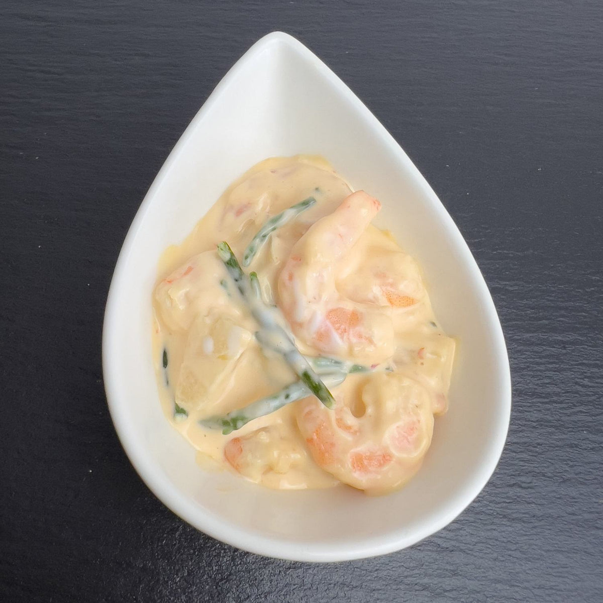 Käptn’s Cocktail in weißer Schale auf schwarzem Schiefer: Garnelen mit Ananas und Meeresspargel in cremigem Dressing.