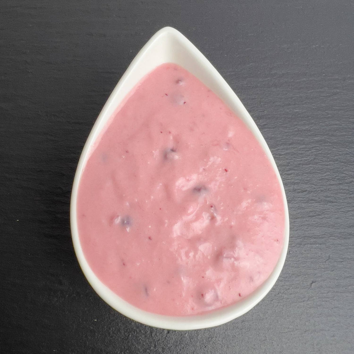 Kronsbeersauce in weißer Schale auf schwarzem Schiefer: rosafarbene Meerrettich-Sahne mit Preiselbeeren.