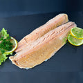 Zwei große heißgeräucherte Lachsforellenfilets mit rosa Fleisch auf Schieferplatte, angerichtet mit Salat, Zitronenscheiben, Dill und Petersilie.