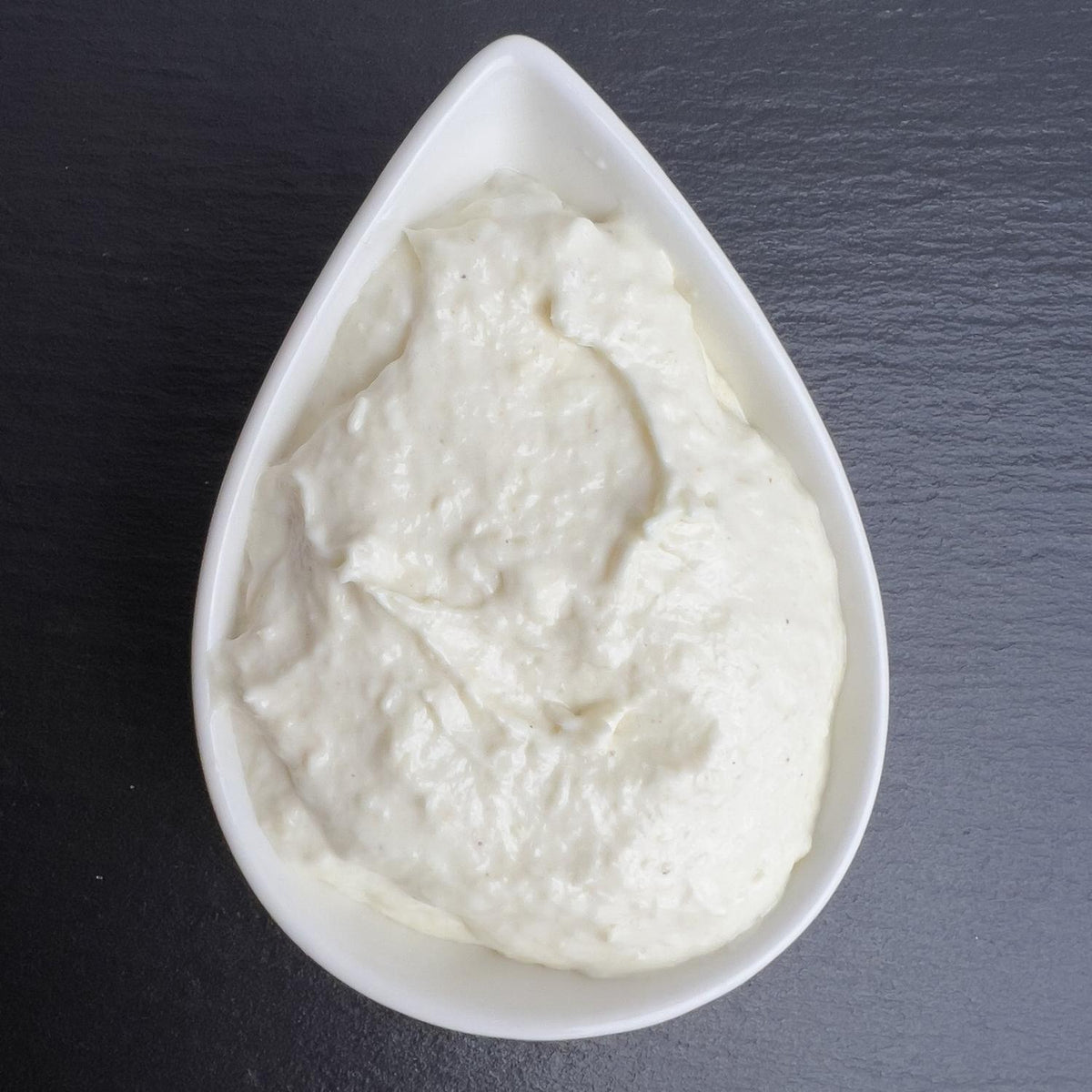 Meerrettich-Sahne-Creme in weißer Schale auf schwarzem Schiefer: cremig-weiße Sahne mit fein geriebenem Meerrettich.