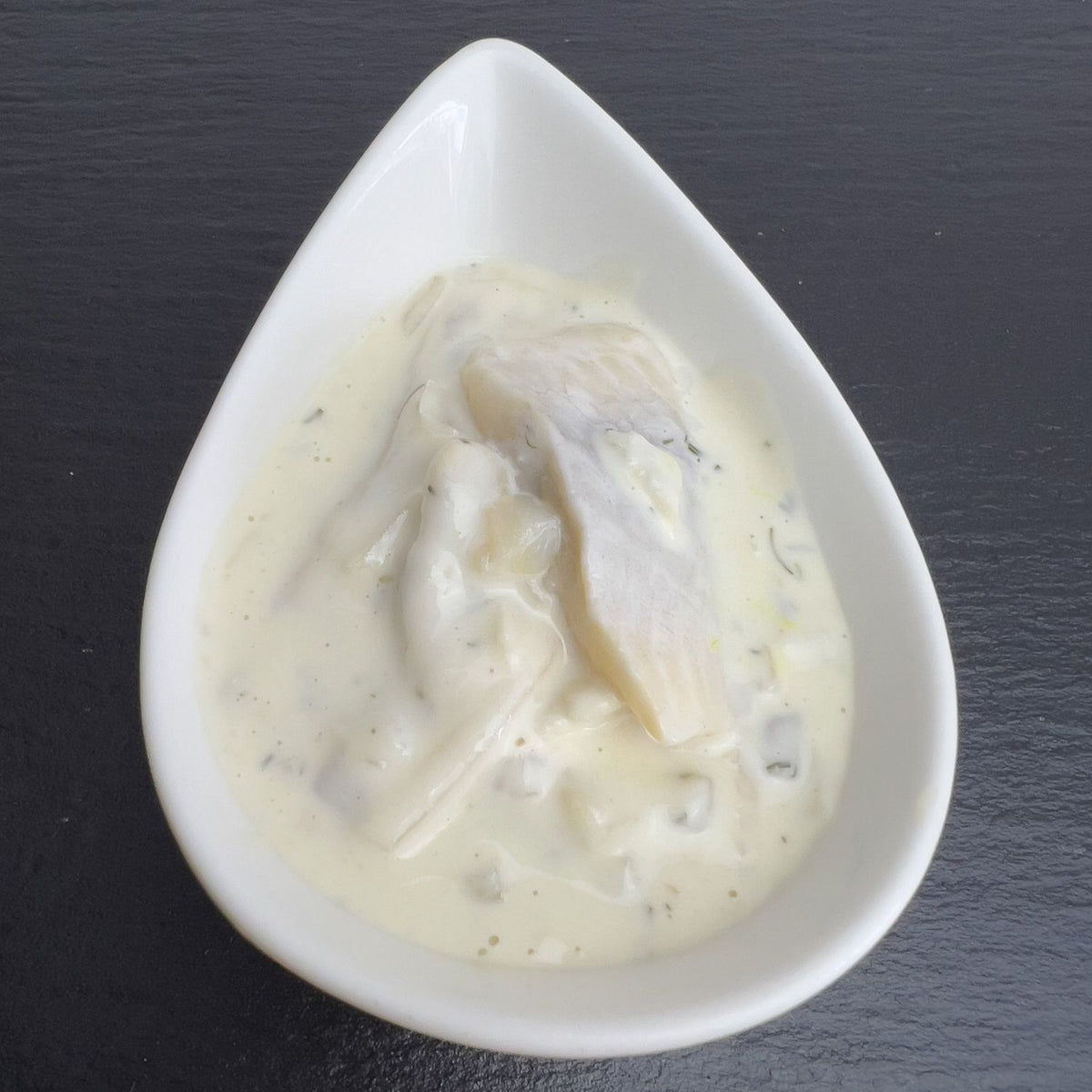 Nordischer Dillsalat in weißer Schale auf schwarzem Schiefer: Matjes und Heringshappen in cremiger Dill-Mayonnaise mit Gewürzgurke.