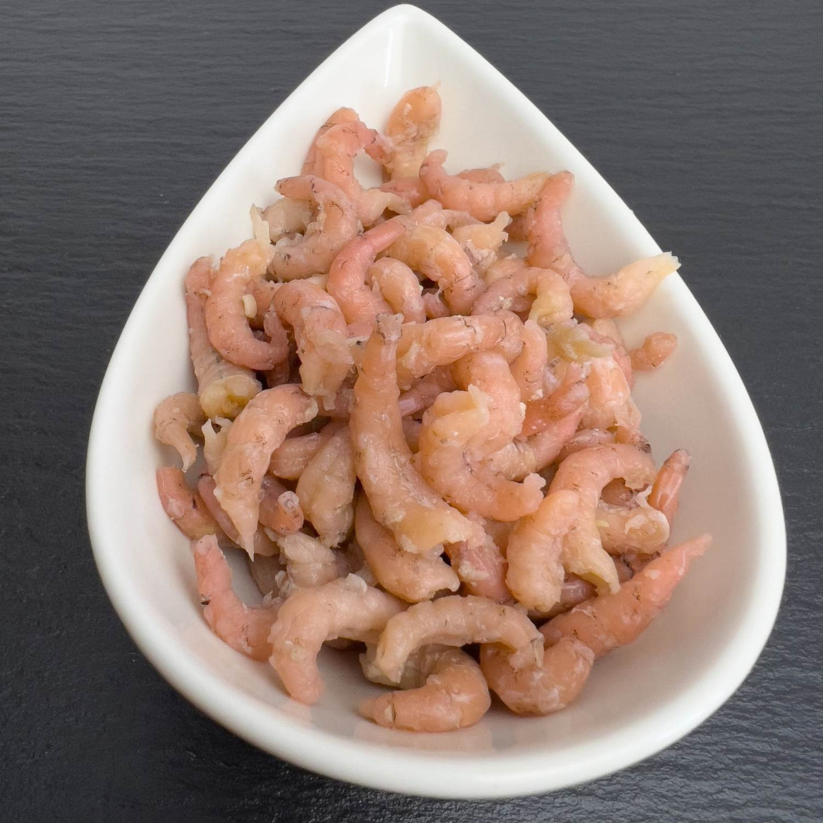 Nordseekrabbenfleisch in weißer Schale auf schwarzem Schiefer: gekochte, geschälte Nordseekrabben, Wildfang aus der Nordsee.