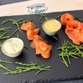 Präsent Küstenschmaus mit Räucherlachs, Graved Lachs, Meerrettich-Sahne-Creme und Senf-Dill-Sauce auf einer Schieferplatte