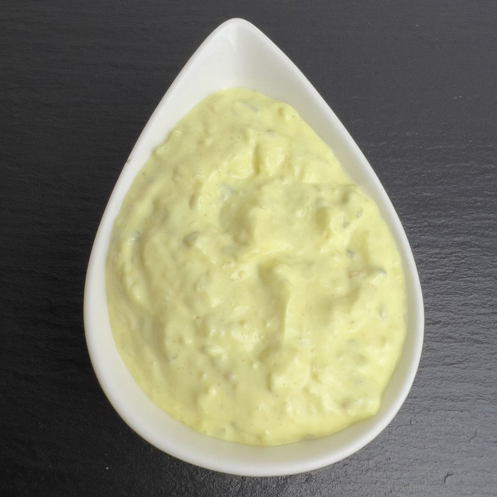Remoulade nach dänischer Art in weißer Schale auf schwarzem Schiefer: gelbe, cremige Remoulade mit Gurkenstückchen.