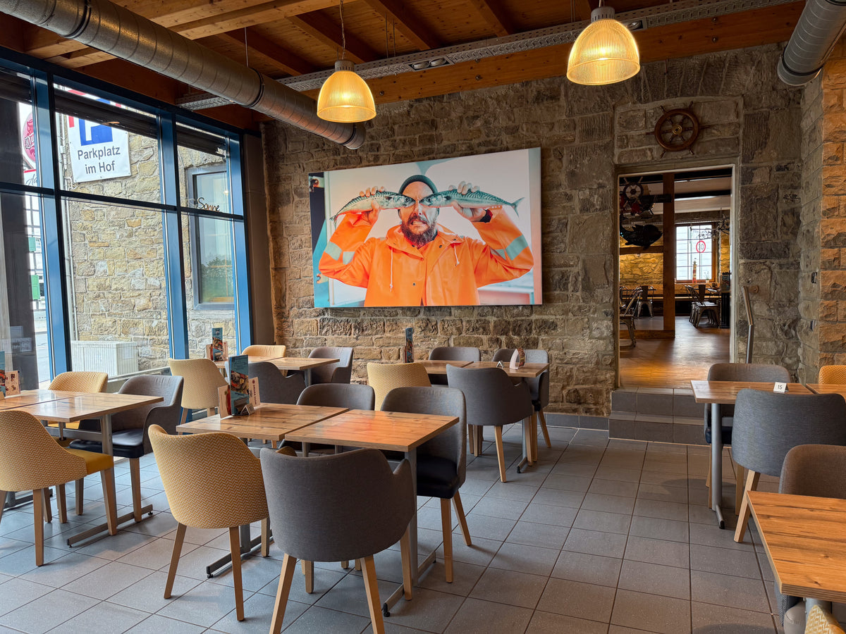 Gastraum des Fisch- und Meeresfrüchte-Restaurants der Wuppertaler Fischkultur mit Natursteinwand, Holztischen und großem Fischer-Wandbild