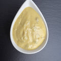 Senf-Dill-Sauce in weißer Schale auf schwarzem Schiefer: cremige, gelbe Sauce mit Dill und Preiselbeeren.