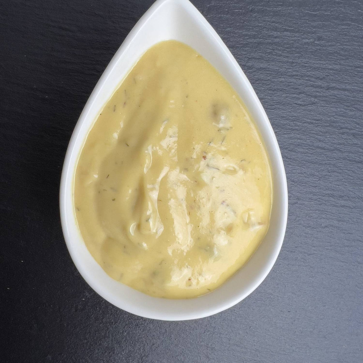 Senf-Dill-Sauce in weißer Schale auf schwarzem Schiefer: cremige, gelbe Sauce mit Dill und Preiselbeeren.