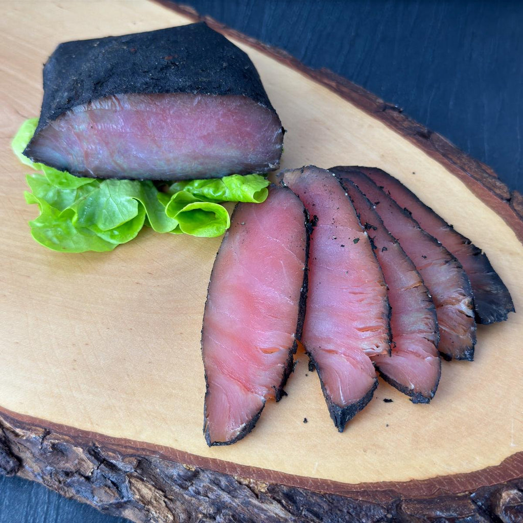 Thunfischfilet Black Edition auf hellem Holzbrett: ein Stück mit tiefschwarzer Hülle auf frischem Salat, davor gefächerte, zartrosa Scheiben.