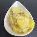 Tiroler Speck-Kartoffelsalat in weißer Schale auf schwarzem Schiefer: Kartoffelscheiben mit Speckwürfeln und Zwiebeln in Öl-Dressing.