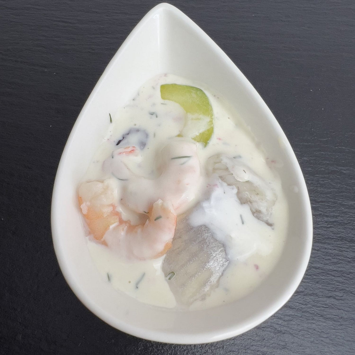 Usedomer Fischerschmaus in weißer Schale auf schwarzem Schiefer: Hering und Garnelen in cremigem Sahne-Dressing mit Gurke und Dill.